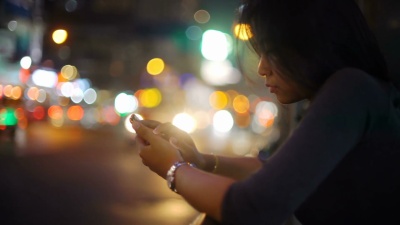 亚洲女孩在公共汽车站附近的夜街使用智能手机