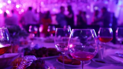 在餐馆或夜总会举行的青年聚会，酒水和食物摆在宴会桌上，背景是跳舞的人的轮廓，舞台灯光和紫色填充，浅景深