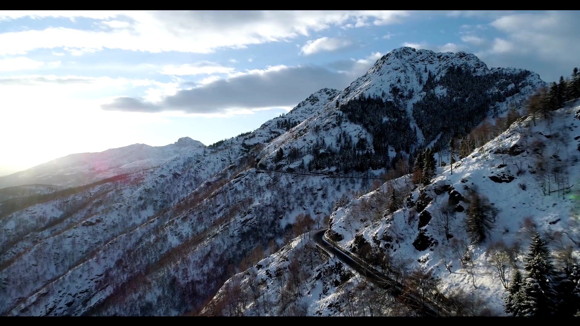 前空中俯视汽车行驶在冬季雪山森林附近的公路上。雪山街道小径建立。日落或日出太阳倒退。全高清无人机飞行建立鞋预览效果