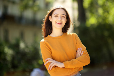 在公园里抱着双臂微笑的年轻女子