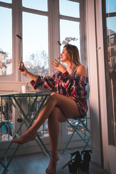 一个年轻的金发女人在出售她的房子旁边吃早餐的生活方式。穿着内衣和睡衣，喝着咖啡，自拍着