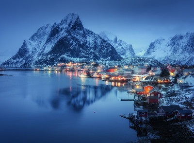 挪威罗浮敦群岛夜晚美丽的勒奈岛。冬季景观有房屋，村庄，照明，雪山在雾中，海，蓝色的云天空倒映在黄昏的