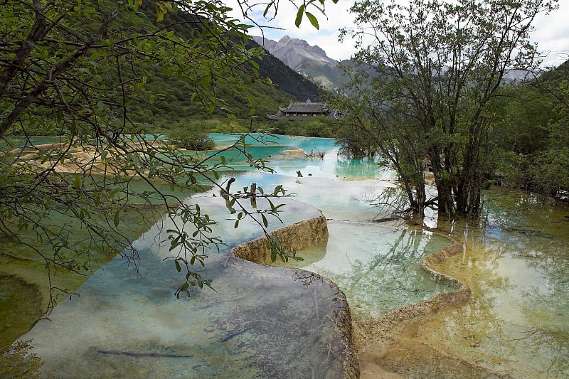 山谷中有石灰华的河岸和明镜般的池塘，背景是古庙