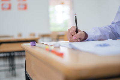 亚洲学生在高中或大学的考场进行考试练习。手持铅笔阅读文件纸在木制课桌上教室，返回学校进行评估测量