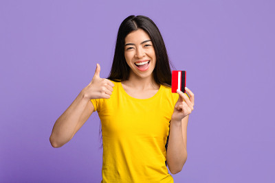 兴奋兴奋的亚洲女人拿着信用卡，竖起大拇指