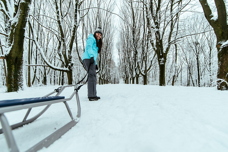 一个女人走过公园，身后拉着雪橇