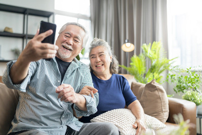 幸福亚洲老人退休夫妇一起在家里客厅的沙发上与家人视频通话，亚洲人用智能手机与家人沟通，居家隔离的理念
