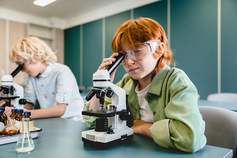 在学校实验室的生物化学课上使用显微镜的学生。科学课的概念