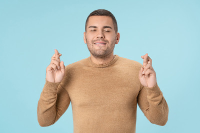 年轻英俊的男子在孤立的蓝色背景与手指交叉许愿