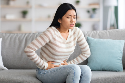 胃疼。生病的亚洲妇女在家中遭受急性腹痛