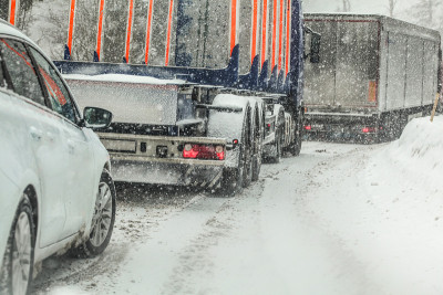 在森林道路交通堵塞期间，汽车在大卡车后面等候，造成暴雪大雪