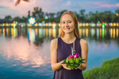 一名女游客手里拿着Loy Krathong，准备把它扔进水里。泰国的水牛节，人们购买鲜花和蜡烛点亮并
