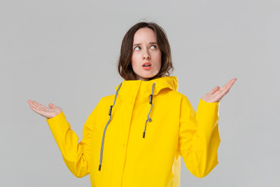 漂亮的黑发女孩正在把衣服穿上黄色的雨衣，看看有没有下雨。准备好迎接坏天气吧。