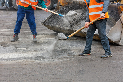 道路工人用铁锹把压碎的旧沥青装进铲运机的铲斗里。