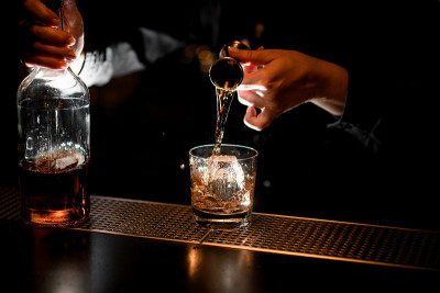 专业的酒保用烧杯将酒倒入加冰的玻璃杯中。
