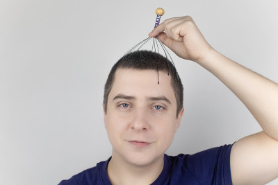 一个白色背景的男人用毛细管按摩器给自己做头部按摩。自助、抗压、放松理念