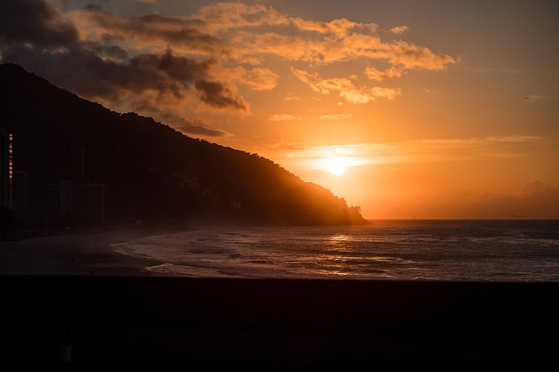 在Sao Conrado，里约热内卢de janeiro的海边，橙色的日落，太阳在山后落山。空旷的海