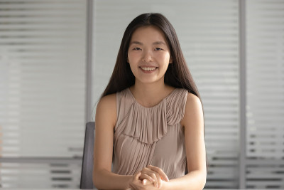 快乐微笑的亚洲女商人看着照相机坐在办公桌前
