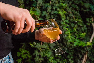 一个男人的手把苹果酒倒进杯子里。一名侍者拿着一杯气泡饮料，背景是一片绿色。