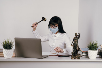 年轻的女律师或法官在疫情期间戴着防护口罩在办公室远程工作。