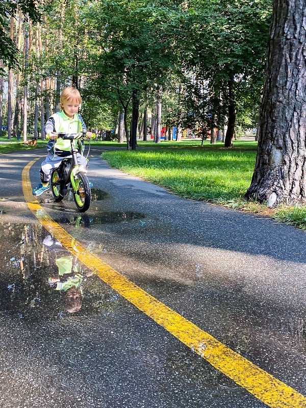 浅肤色的孩子在雨后的公园里骑自行车。