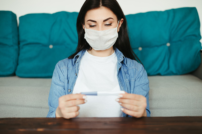 妇女在医疗口罩与怀孕测试