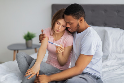 不开心的黑人丈夫在床上安慰怀孕测试呈阴性的年轻妻子