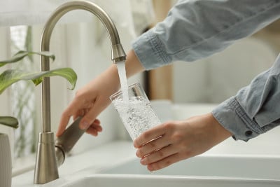 一名妇女从家里的水龙头往玻璃杯里注水