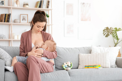 母乳喂养的概念。年轻妇女在家沙发上给蹒跚学步的婴儿哺乳