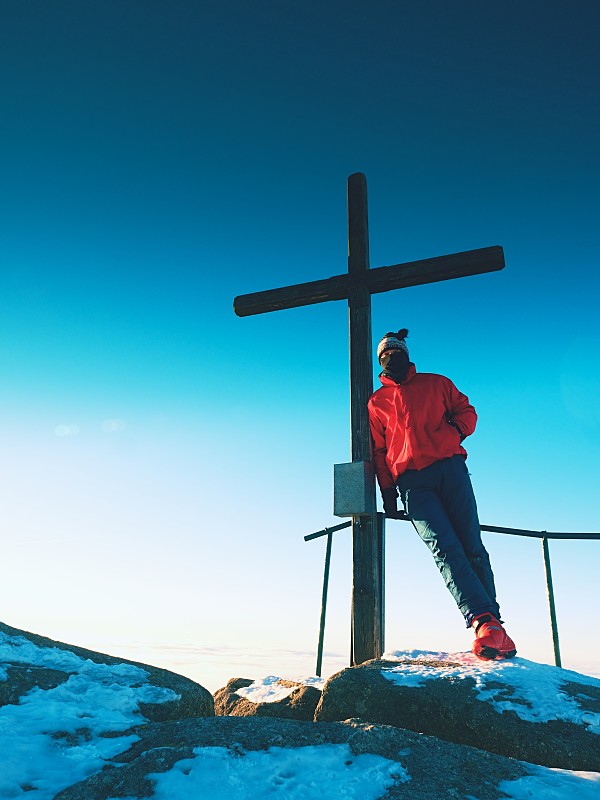 登山者在山顶上穿着暖和的衣服和木制十字架。