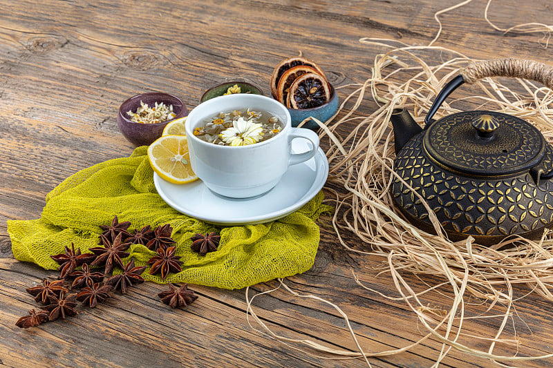 铸造茶壶中的甘菊茶。洋甘菊茶杯，中国古代铸铁茶壶，柠檬和八角放在木桌上。