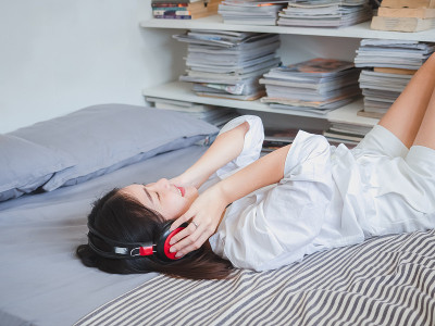 一个亚洲女孩戴着耳机在床上听音乐