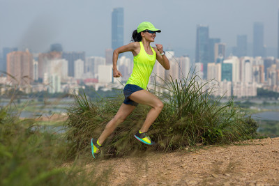 女超级马拉松运动员在现代城市旁边的山上跑步