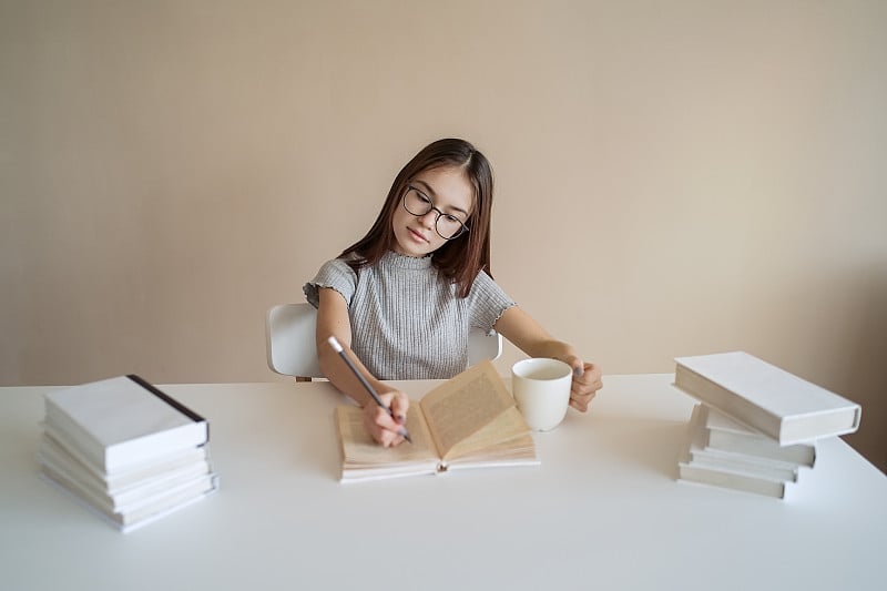 十几岁的女孩坐在桌前，拿着书做作业