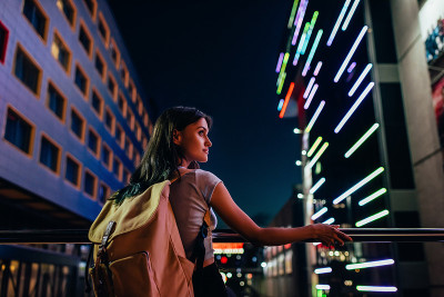 美丽沉思的女人背着背包看着夜晚的城市街道