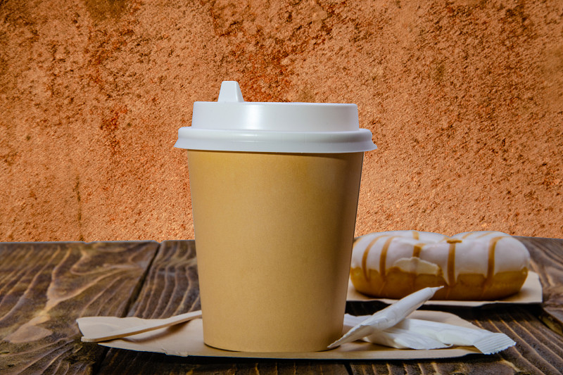 Paper cup for coffee. Wooden table. Orange backgro