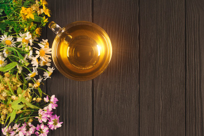 用菩提树、甘菊、三叶草和金丝桃制成的新鲜草本茶，在透明的玻璃杯中，周围有花和叶子，在带有copysp