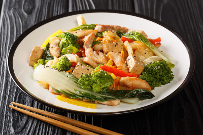 黑色背景盘上的亚洲炒鸡、豆腐和时令蔬菜。水平