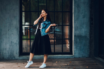 时尚的年轻女子在时髦的休闲服装享受最喜爱的音乐在现代耳机在空闲时间。嬉皮女孩用耳机连接到数字智能手机