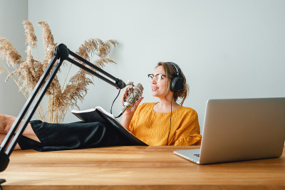 女人坐着，他的脚放在他的桌子上，录制直播播客。女播客流她的声音到麦克风在家里工作室“t”n
