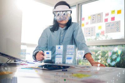 亚洲女性使用增强现实(ar)眼镜模拟ux UI设计在办公室的桌子上工作。虚拟现实的发展过程概念