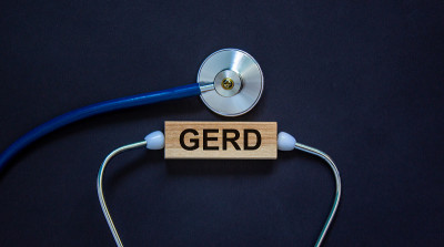 带有“GERD”字样的木块和黑色背景上的听诊器。医学概念。