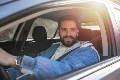 微笑英俊的男人开着他的车，看着窗外。手放在方向盘上