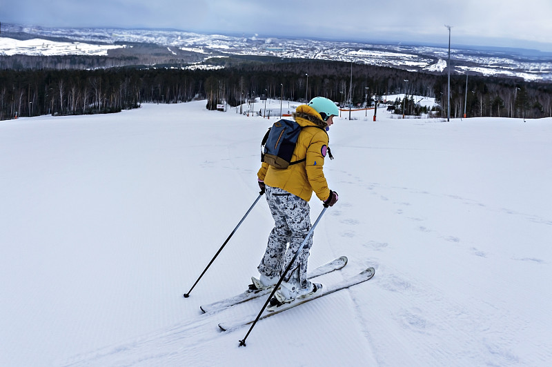 年轻女子穿着黄色夹克，戴着滑雪头盔在山坡上滑雪，冬季运动，户外高山滑雪活动，健康的生活方式