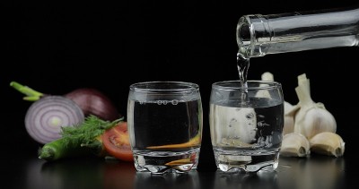 将伏特加从酒瓶中倒入小酒杯中。背景用蔬菜