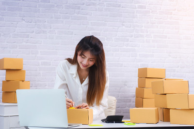 女性企业主在家庭办公室工作场所的包装盒上写地址。网上购物中小企业创业者或自由职业者的工作理念。