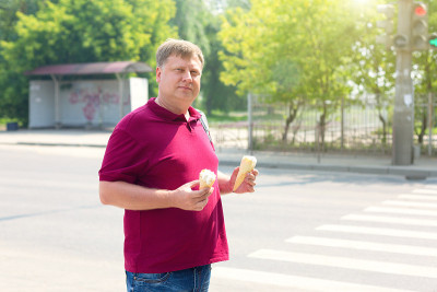 一个有肥胖倾向的成年男子在一个阳光明媚的日子在城市街道上喝两杯冰淇淋