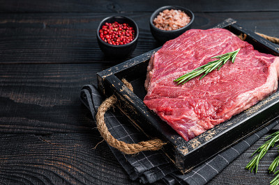 生牛肉片牛排在一个木制托盘与香草。黑色木制背景。前视图。本空间