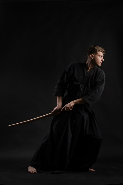 剑道大师穿着传统的日本和服正在练习武术与shinai竹剑在一个黑色的工作室背景
