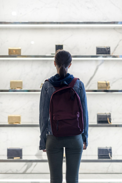 一个女人拿着袋子站在商店橱窗前。后视图。